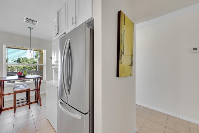 kitchen with stainless steel fridge, white cabinetry, pendant lighting, and light tile patterned flooring