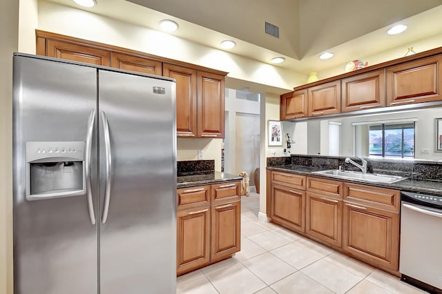 kitchen with appliances with stainless steel finishes, light tile patterned flooring, dark stone countertops, and sink