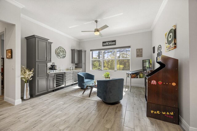 sitting room with ceiling fan, beverage cooler, light wood-type flooring, and ornamental molding