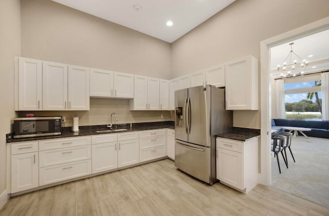 kitchen featuring white cabinets, sink, appliances with stainless steel finishes, a notable chandelier, and light hardwood / wood-style floors