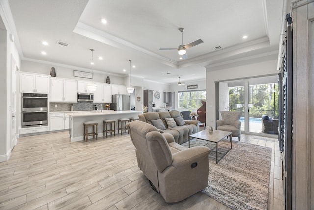 living room featuring a raised ceiling, ornamental molding, ceiling fan, and light hardwood / wood-style flooring