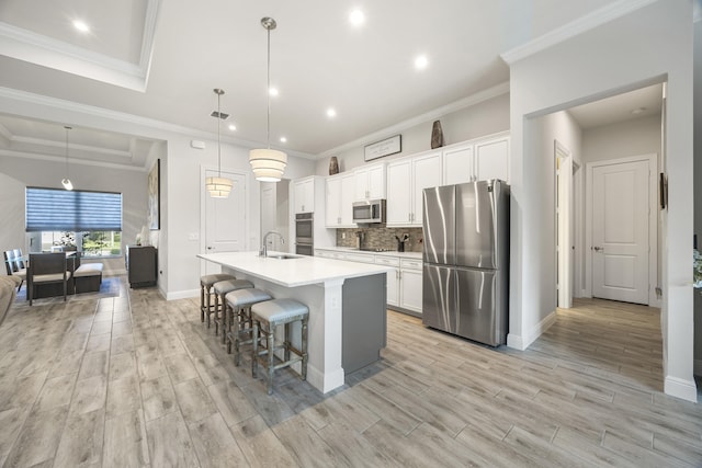 kitchen with a kitchen island with sink, stainless steel appliances, white cabinets, and decorative light fixtures