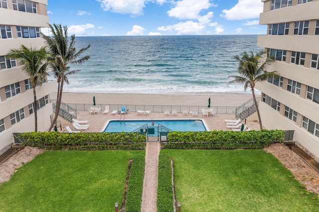 view of pool with a water view, a lawn, and a beach view