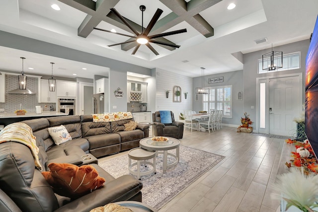 living room with coffered ceiling, beamed ceiling, ceiling fan with notable chandelier, and light wood-type flooring