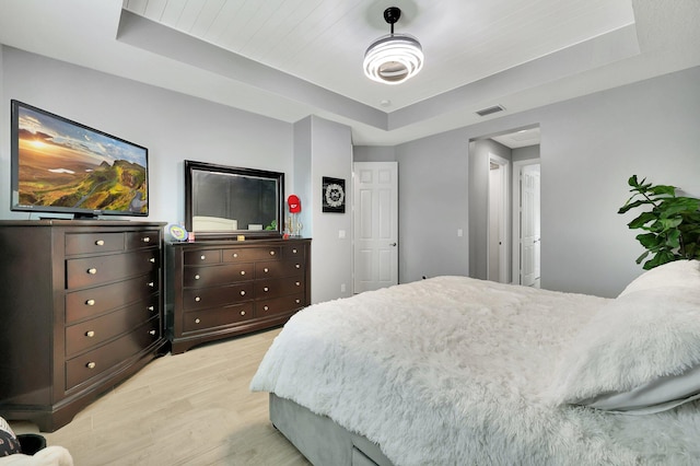 bedroom with light wood-type flooring and a raised ceiling