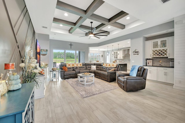 living room with ceiling fan with notable chandelier, beamed ceiling, coffered ceiling, and light hardwood / wood-style flooring