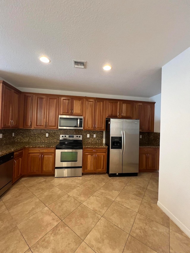 kitchen with appliances with stainless steel finishes, a textured ceiling, tasteful backsplash, and dark stone counters