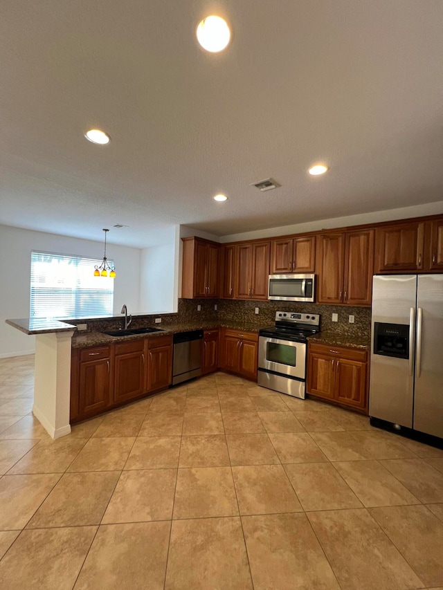 kitchen featuring kitchen peninsula, dark stone counters, sink, decorative light fixtures, and appliances with stainless steel finishes