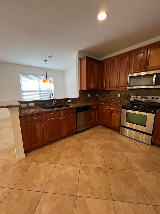 kitchen featuring kitchen peninsula, dark stone countertops, sink, pendant lighting, and appliances with stainless steel finishes