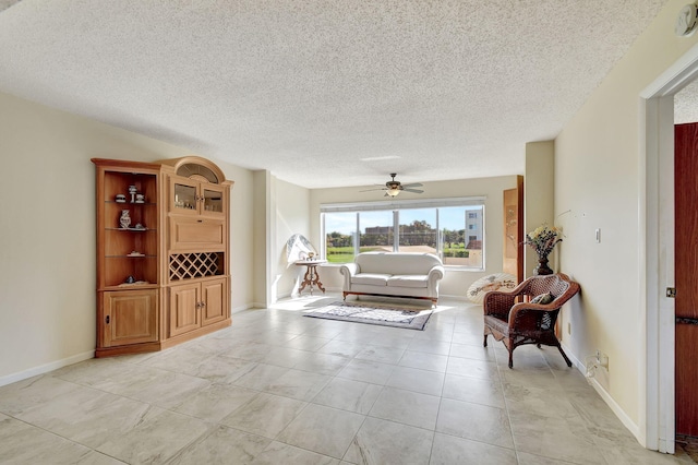 living area featuring light tile patterned floors, ceiling fan, baseboards, and a textured ceiling