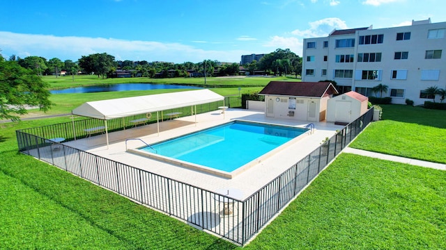 view of swimming pool featuring a water view, a storage unit, and a lawn