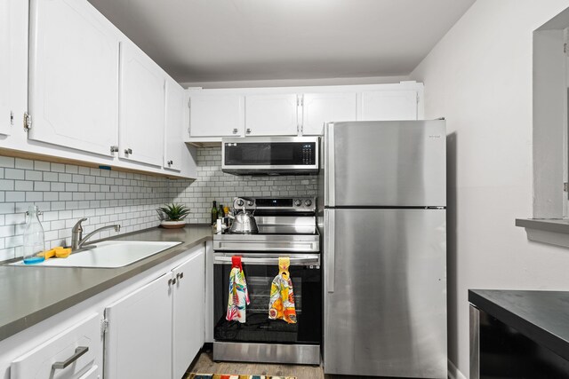 kitchen featuring stainless steel appliances, a sink, white cabinets, backsplash, and dark countertops