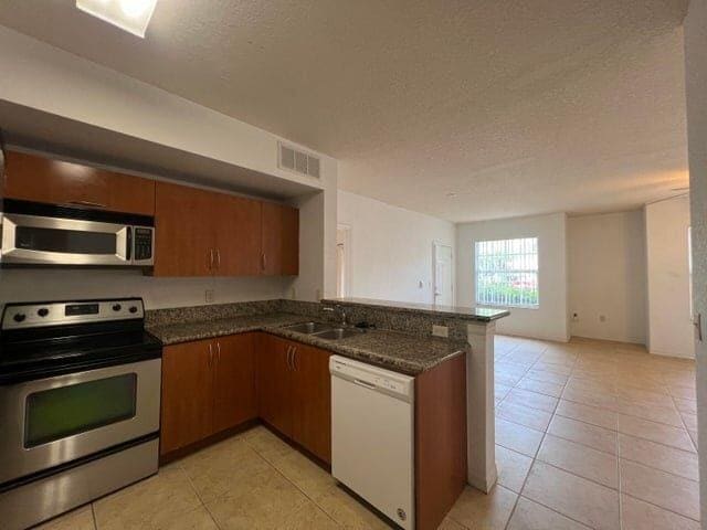 kitchen featuring dark stone countertops, light tile patterned flooring, sink, and stainless steel appliances