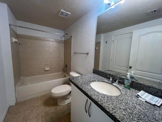 full bathroom with vanity, a textured ceiling, tiled shower / bath combo, tile patterned flooring, and toilet