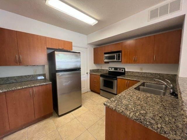 kitchen featuring light tile patterned floors, stainless steel appliances, a textured ceiling, dark stone counters, and sink