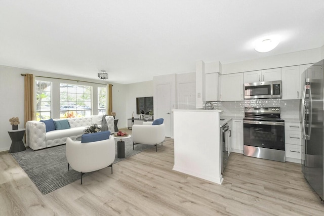 kitchen with decorative backsplash, white cabinets, appliances with stainless steel finishes, and light hardwood / wood-style flooring