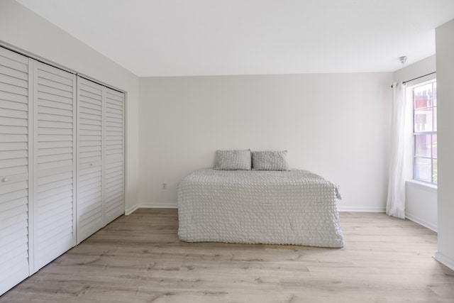 bedroom with a closet, light hardwood / wood-style floors, and multiple windows