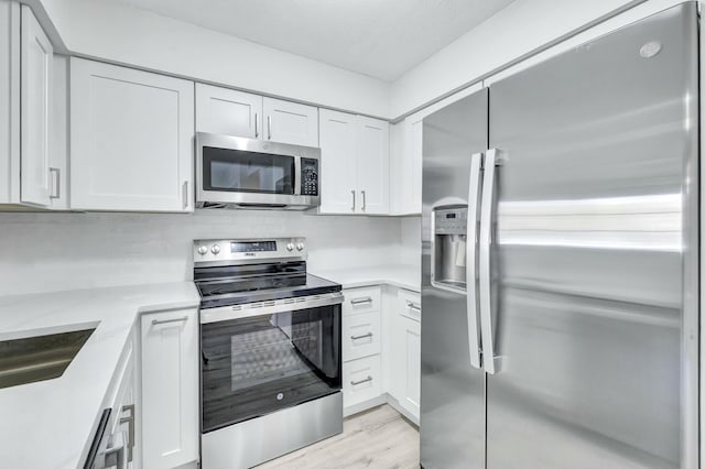 kitchen with appliances with stainless steel finishes, sink, light hardwood / wood-style floors, and white cabinets