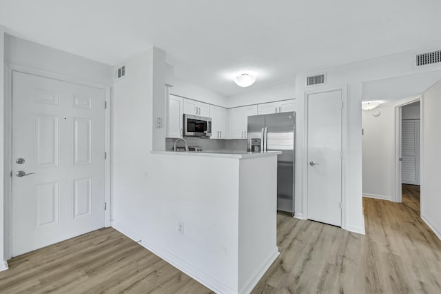 kitchen featuring appliances with stainless steel finishes, light hardwood / wood-style flooring, white cabinets, and kitchen peninsula