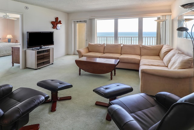 living room featuring a water view, ceiling fan, carpet, and a textured ceiling