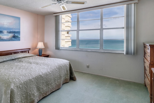 carpeted bedroom with a water view, ceiling fan, and a textured ceiling