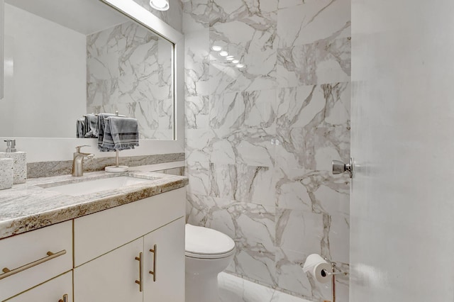 bathroom featuring vanity, tile walls, and toilet