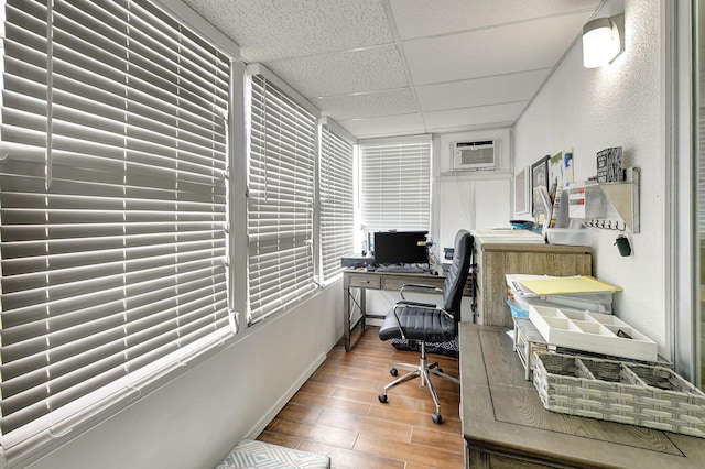 home office with a drop ceiling, hardwood / wood-style floors, and a wall mounted air conditioner