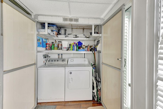 laundry room with wooden walls, wood-type flooring, and washing machine and dryer