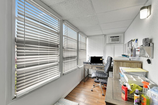 office area with a wall mounted air conditioner, a drop ceiling, and light hardwood / wood-style floors