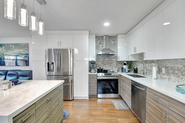 kitchen with sink, white cabinets, wall chimney exhaust hood, stainless steel appliances, and decorative light fixtures