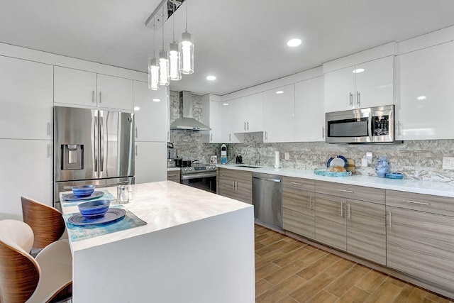 kitchen with appliances with stainless steel finishes, white cabinetry, wall chimney exhaust hood, decorative light fixtures, and sink