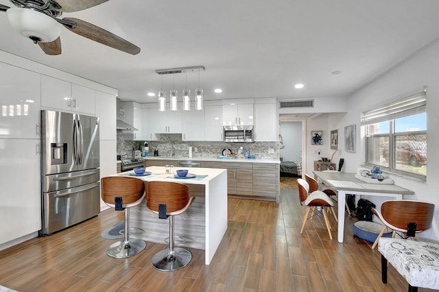 kitchen featuring light wood-type flooring, white cabinetry, hanging light fixtures, a kitchen island, and stainless steel appliances