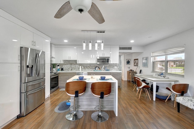 kitchen with decorative light fixtures, hardwood / wood-style flooring, stainless steel appliances, and white cabinetry