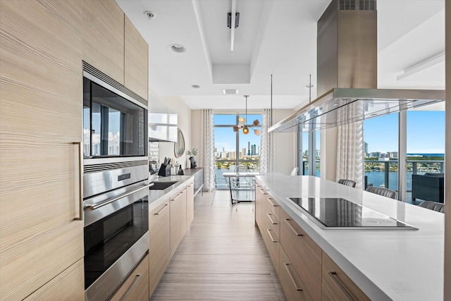 kitchen featuring light brown cabinets, decorative light fixtures, ventilation hood, black electric stovetop, and a water view