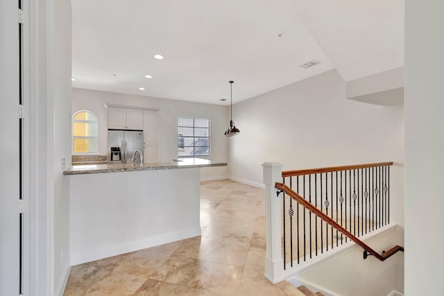 kitchen with stainless steel refrigerator with ice dispenser, white cabinetry, light stone countertops, and plenty of natural light