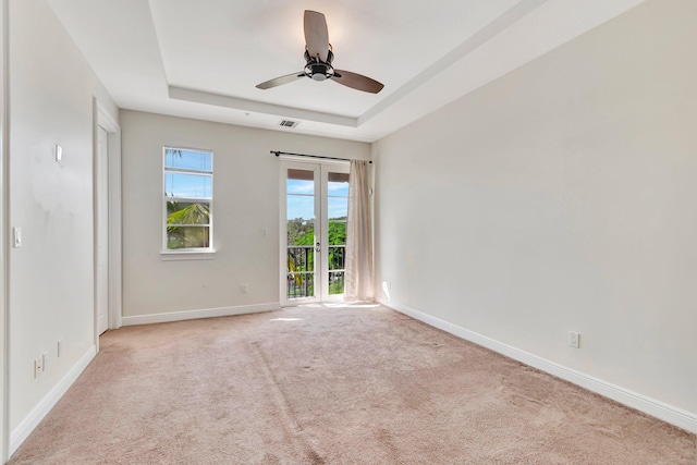 spare room with ceiling fan, light colored carpet, and a raised ceiling