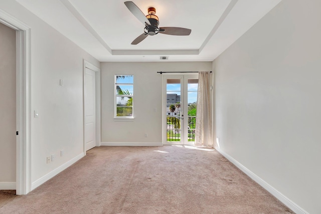 empty room with ceiling fan, light colored carpet, and a raised ceiling