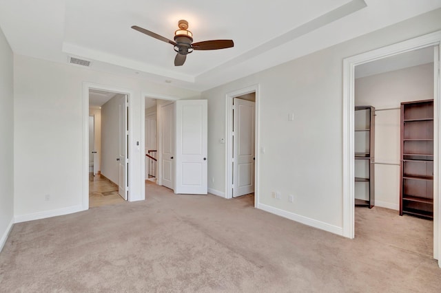 unfurnished bedroom featuring a tray ceiling, ceiling fan, and light colored carpet