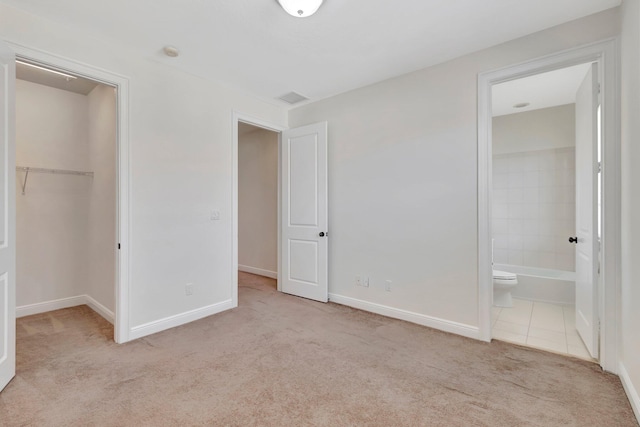 unfurnished bedroom featuring a spacious closet, ensuite bath, light colored carpet, and a closet