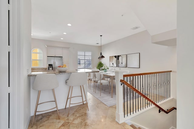 kitchen featuring pendant lighting, white cabinetry, kitchen peninsula, light stone countertops, and stainless steel fridge