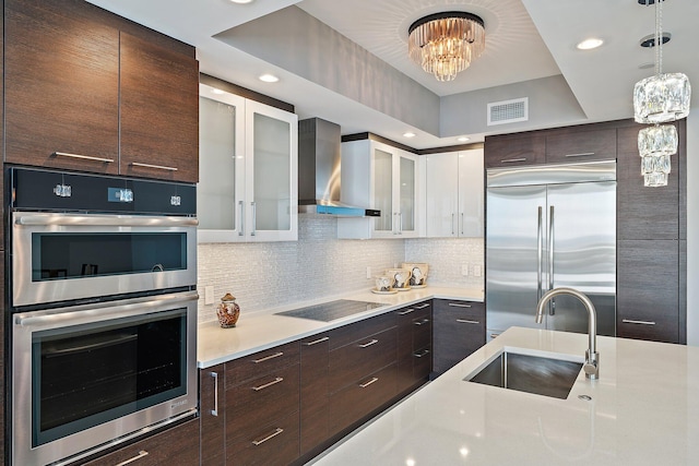 kitchen featuring appliances with stainless steel finishes, white cabinetry, sink, wall chimney range hood, and a notable chandelier