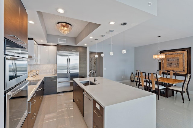 kitchen featuring an island with sink, white cabinets, stainless steel appliances, an inviting chandelier, and sink