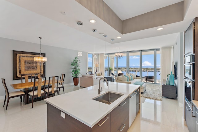 kitchen featuring a notable chandelier, a kitchen island with sink, sink, and a water view