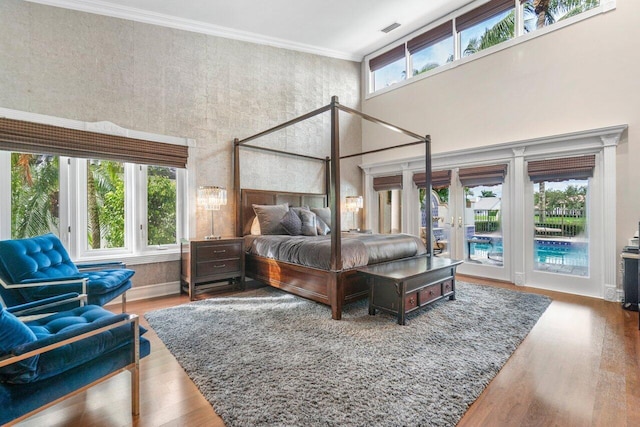 bedroom featuring hardwood / wood-style floors, ornamental molding, a towering ceiling, and access to exterior