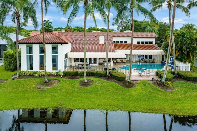 rear view of property featuring a lawn, a water view, a fenced in pool, and a patio area