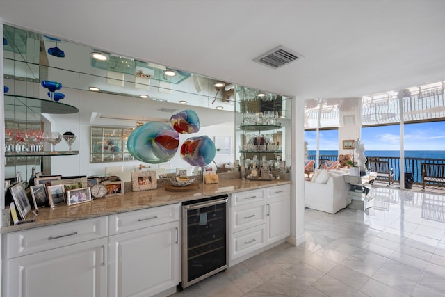 bar with a water view, white cabinetry, beverage cooler, and light stone counters