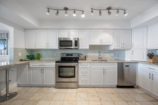 kitchen with light stone counters, sink, tasteful backsplash, white cabinetry, and appliances with stainless steel finishes