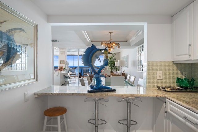 kitchen with light stone countertops, kitchen peninsula, white cabinetry, and a breakfast bar area