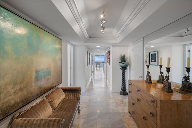 hall with a raised ceiling and ornamental molding