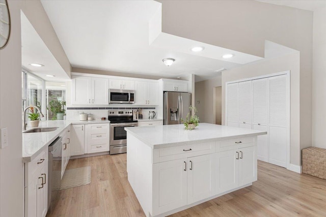 kitchen featuring sink, appliances with stainless steel finishes, a kitchen island, light hardwood / wood-style floors, and white cabinets